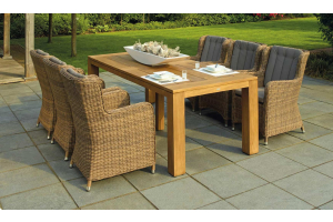 woven furniture and wood dining table sitting on a grey square patio with grass in the background