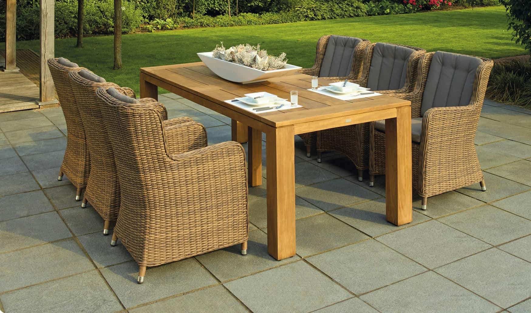 woven furniture and wood dining table sitting on a grey square patio with grass in the background